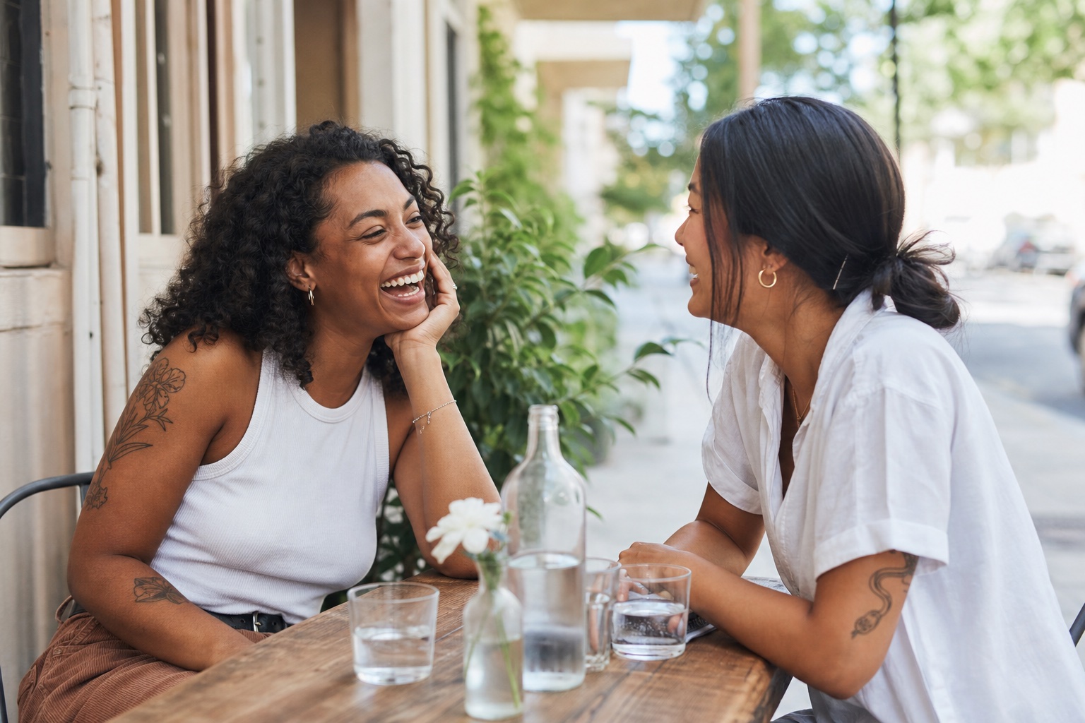 Two women laughing together on a sunny café date